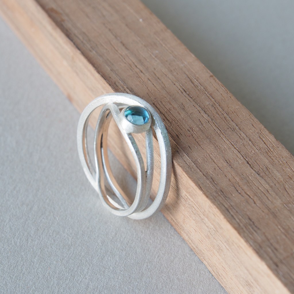 Anillo Etapas de plata con topacio azul apoyado en madera